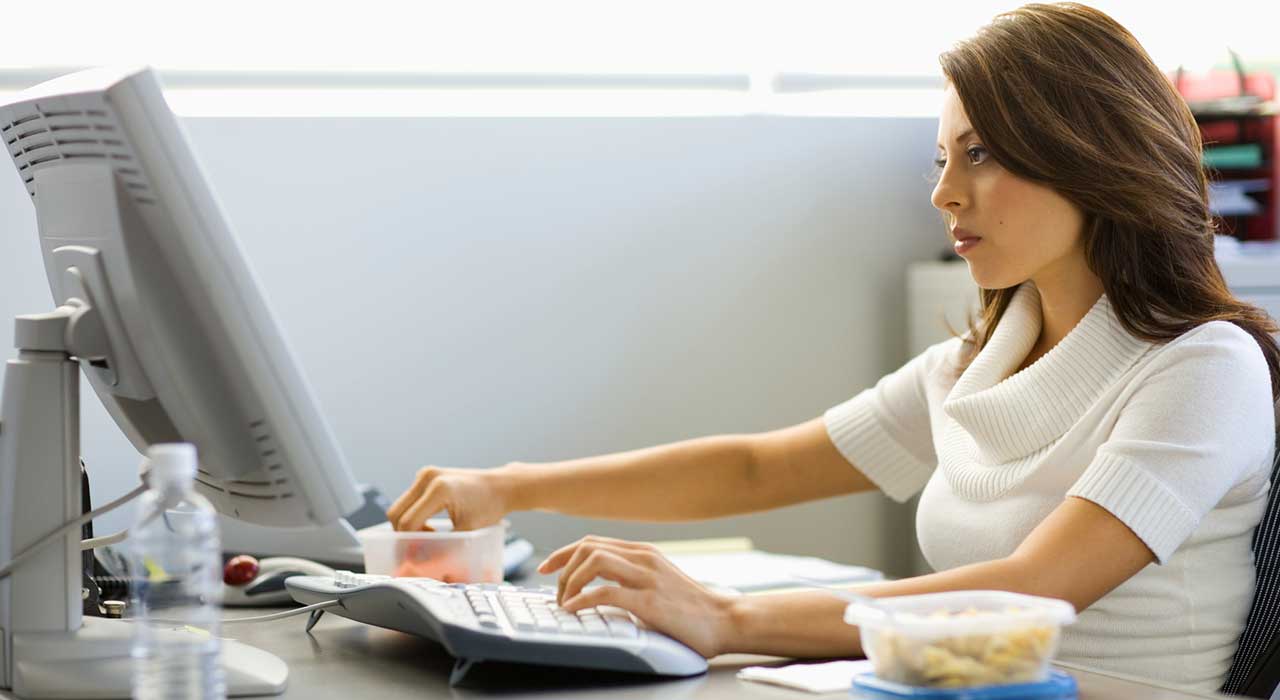 woman sitting at a desk at work on the computer with snacks
