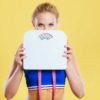 fit woman holding up a weight scale with a yellow background