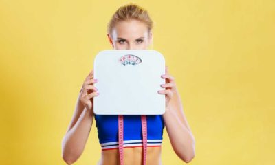 fit woman holding up a weight scale with a yellow background