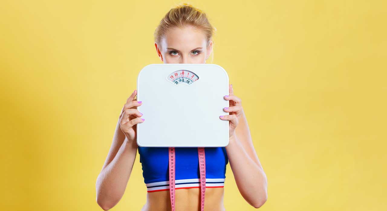 fit woman holding up a weight scale with a yellow background
