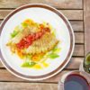 a plate of food on a wooden table with a bottle of wine and a glass