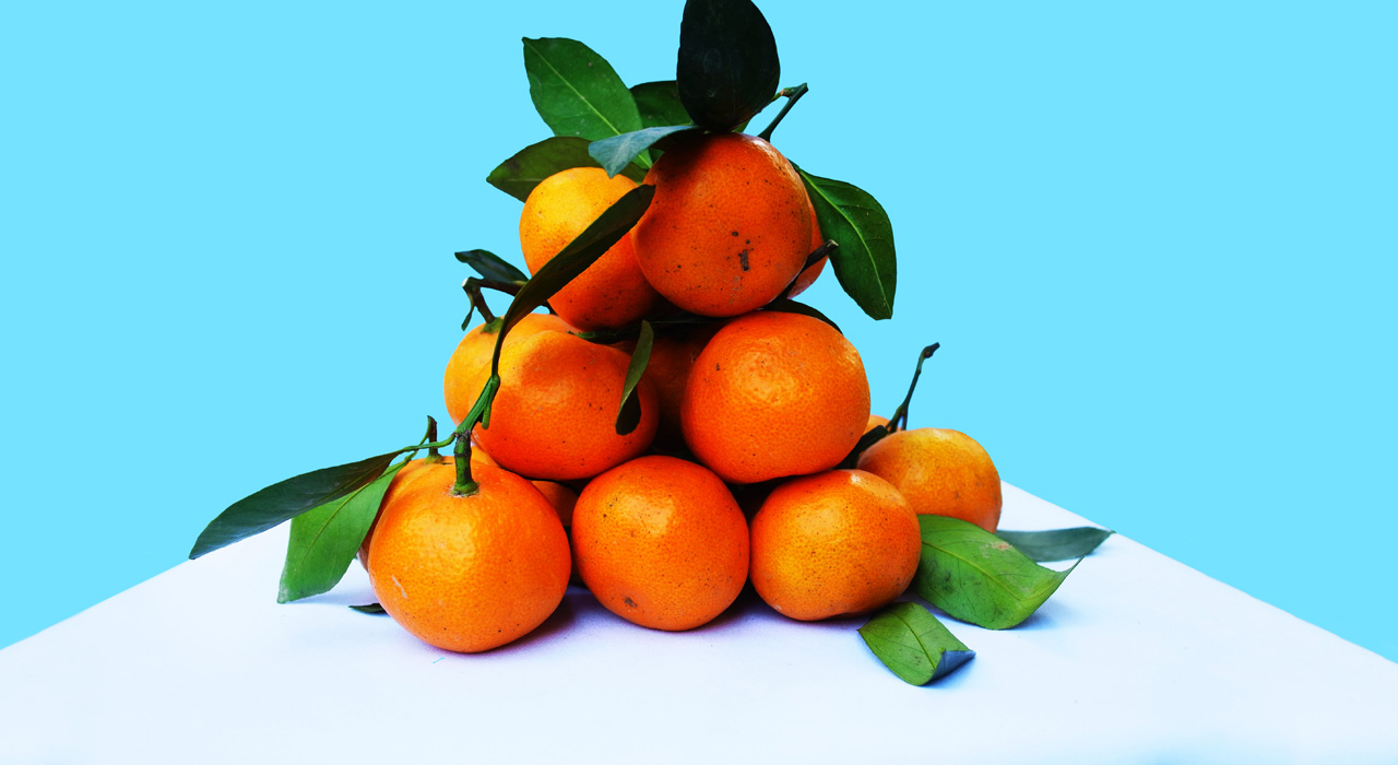 a pile of oranges on a table corner with a light blue background