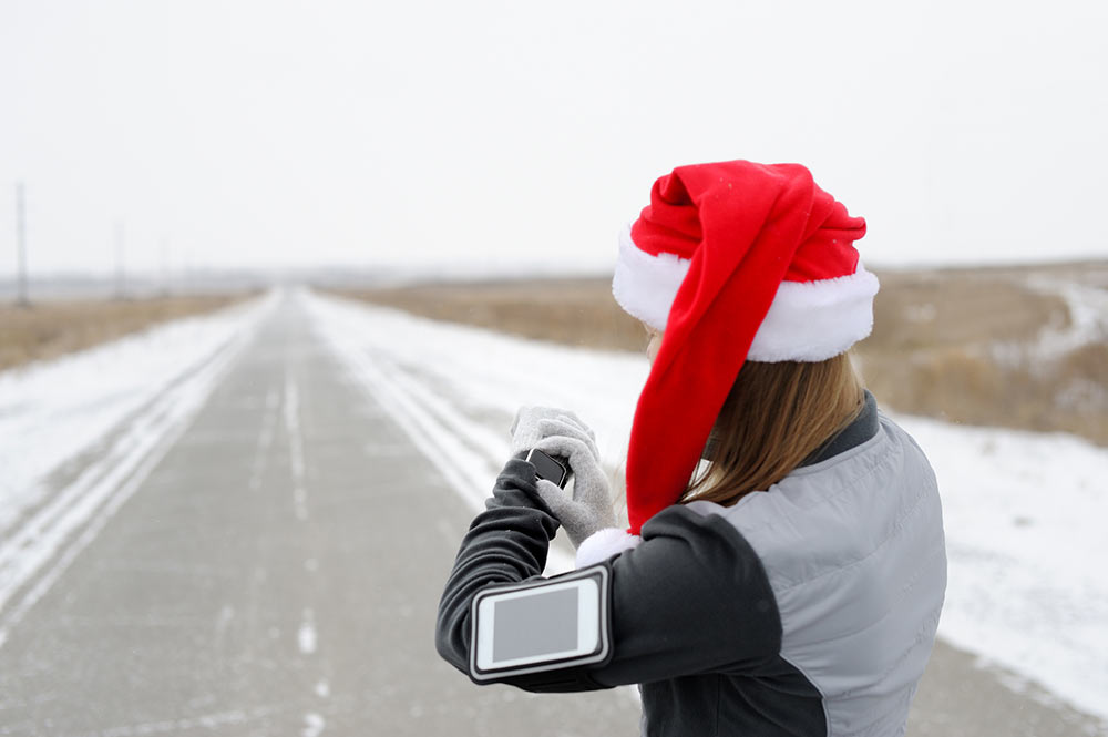 woman wearing a santas hat looking at her watch on an empty countryside road