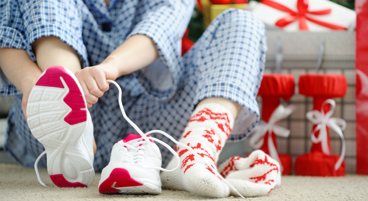 woman in pyjamas putting on running shoes next to presents