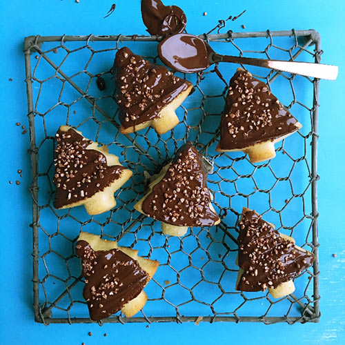 chocolate christmas tree cakes on a baking tray with a chocolate covered spoon