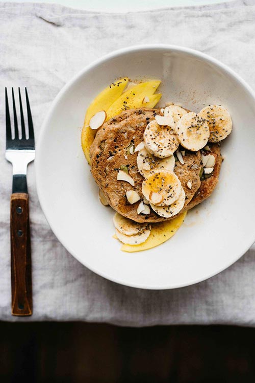 pancakes with seeds and chopped bananas on a white plate with a fork