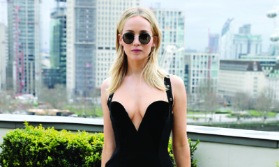 Jennifer Lawrence posing in a black dress and sunglasses on a balcony