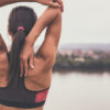 a woman stretching out her arm and shoulder outside next to a river