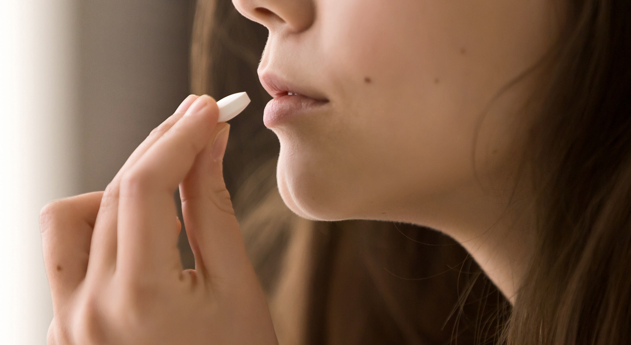 woman holding a vitamin tablet close to her mouth