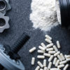 dumbbell weight surrounded by gym supplement powder and pills