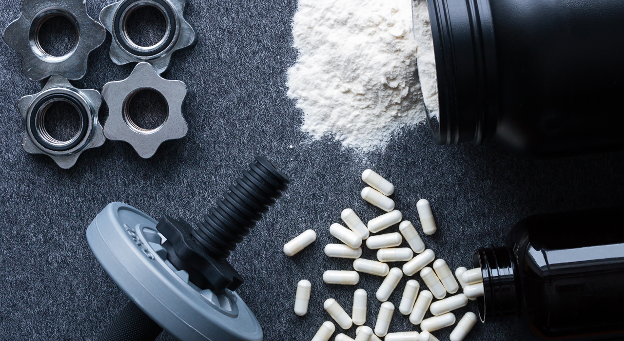 dumbbell weight surrounded by gym supplement powder and pills