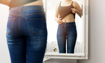 woman pulling her top up looking at her belly in the mirror