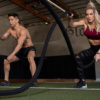 fit man and fit woman performing battle rope exercises