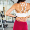 fit woman in the gym holding her lower back due to a pain