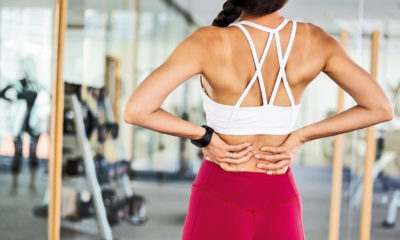 fit woman in the gym holding her lower back due to a pain