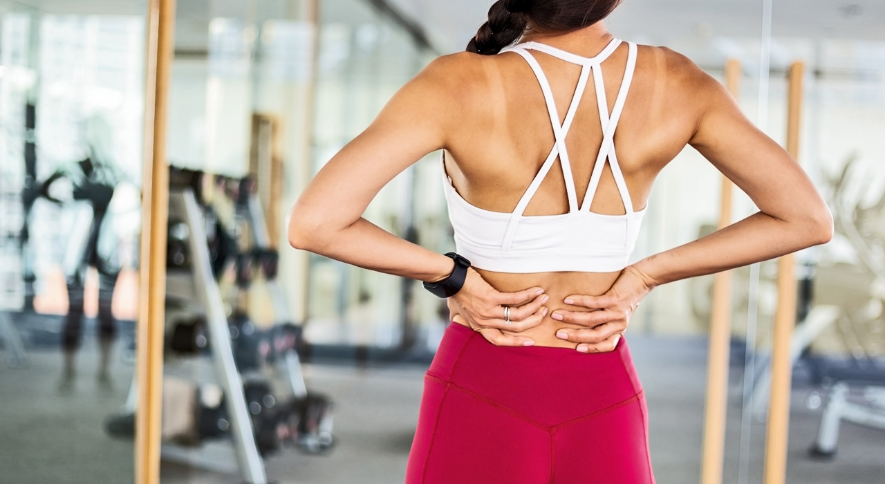 fit woman in the gym holding her lower back due to a pain