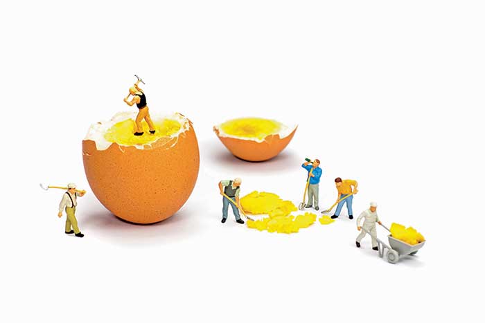 miniature builder figures working on a hard boiled egg that's broken in two