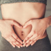 a woman holding her hands infront of her gut in a love heart shape