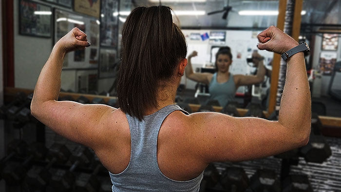 fit woman flexing biceps in the mirror at the gym