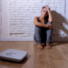 woman sitting against a wall next to some scales looking stressed