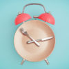 an alarm clock graphic with the face as a plate and the hands as a knife and fork on a light blue background