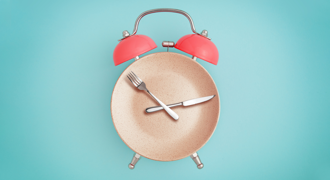an alarm clock graphic with the face as a plate and the hands as a knife and fork on a light blue background