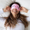 woman in bed smiling with sleep eye mask