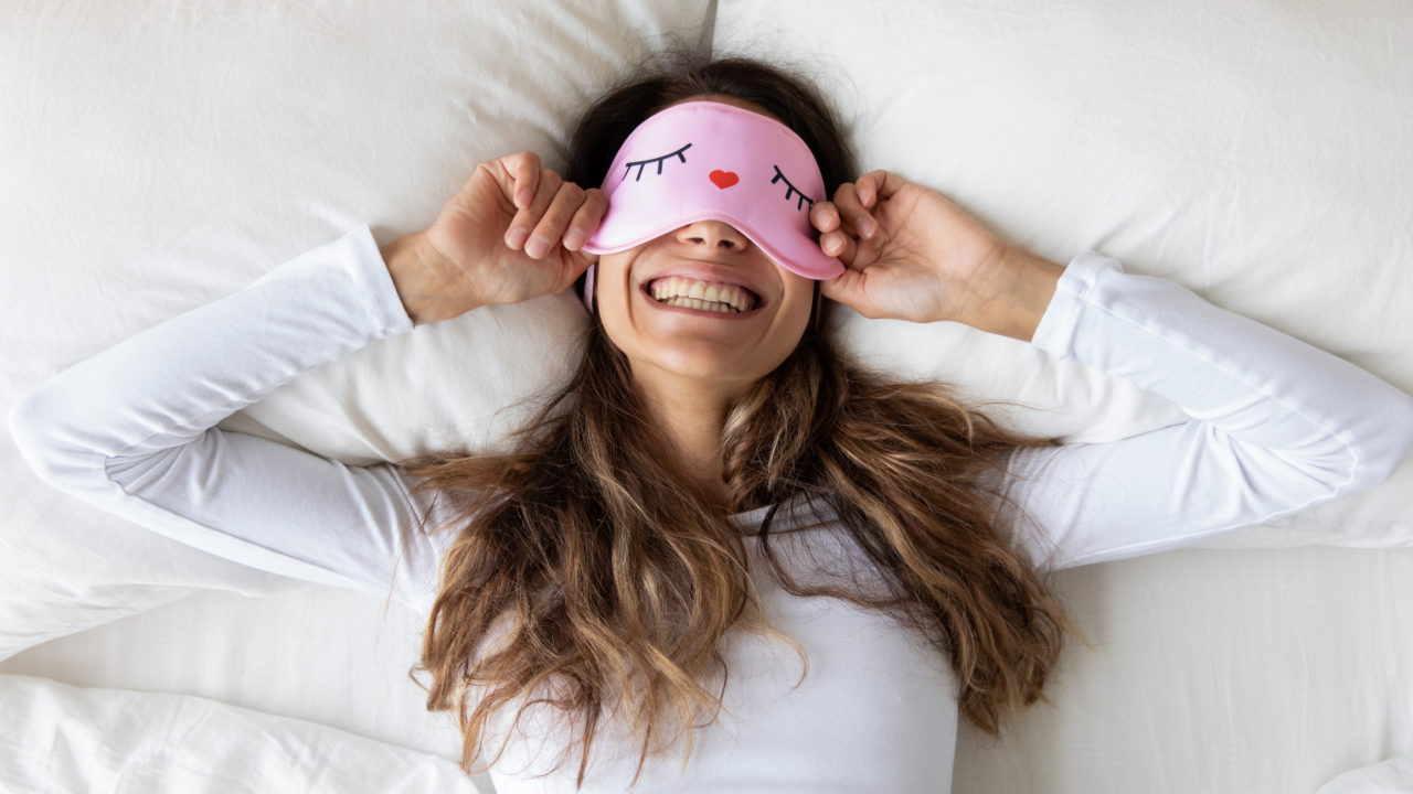 woman in bed smiling with sleep eye mask