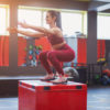 Side view of cheerful middle-aged woman working out with jump box in modern gym
