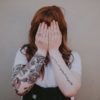 woman holding her hands over her face with arm tattoos