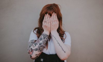 woman holding her hands over her face with arm tattoos