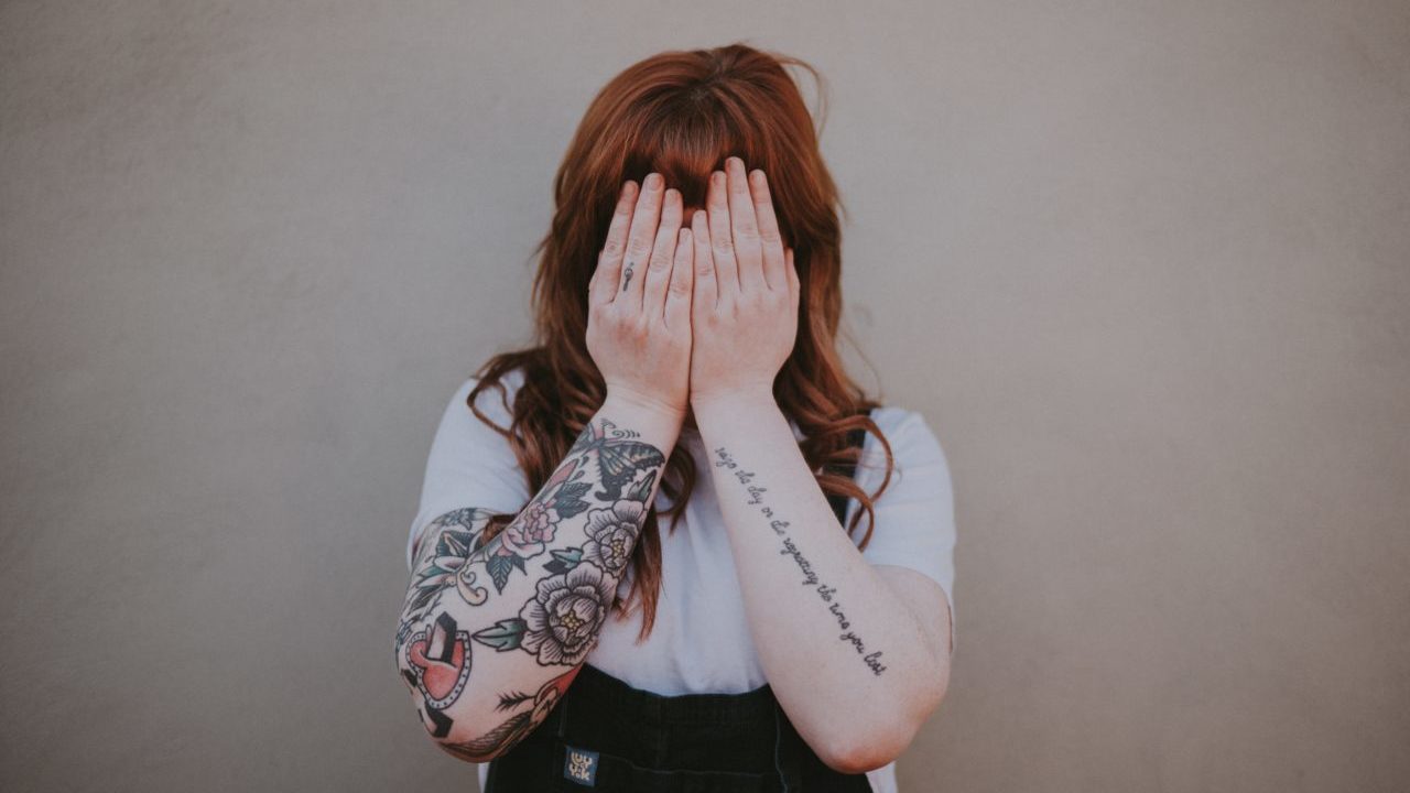 woman holding her hands over her face with arm tattoos