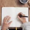 woman writing down in her journal with croissant and coffee