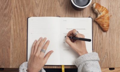 woman writing down in her journal with croissant and coffee