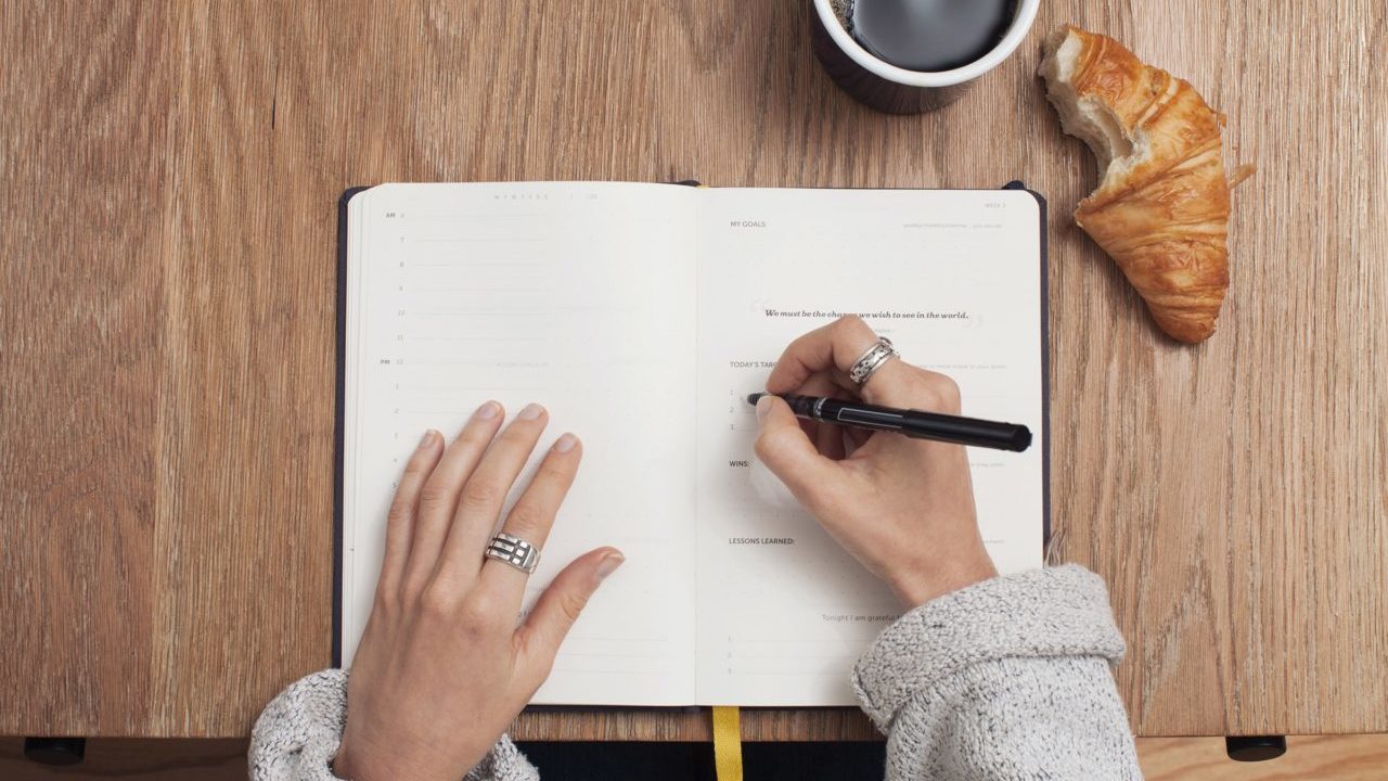 woman writing down in her journal with croissant and coffee