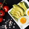 tomatoes on a table next to avocado and eggs on a plate