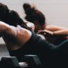 two women performing bodyweight exercises next to dumbbells