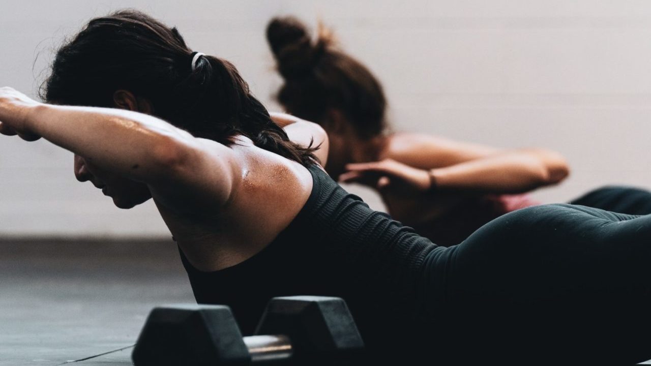 two women performing bodyweight exercises next to dumbbells