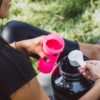 woman dressed in black gym gear scooping protein into pink protein shaker