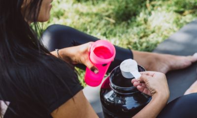 woman dressed in black gym gear scooping protein into pink protein shaker